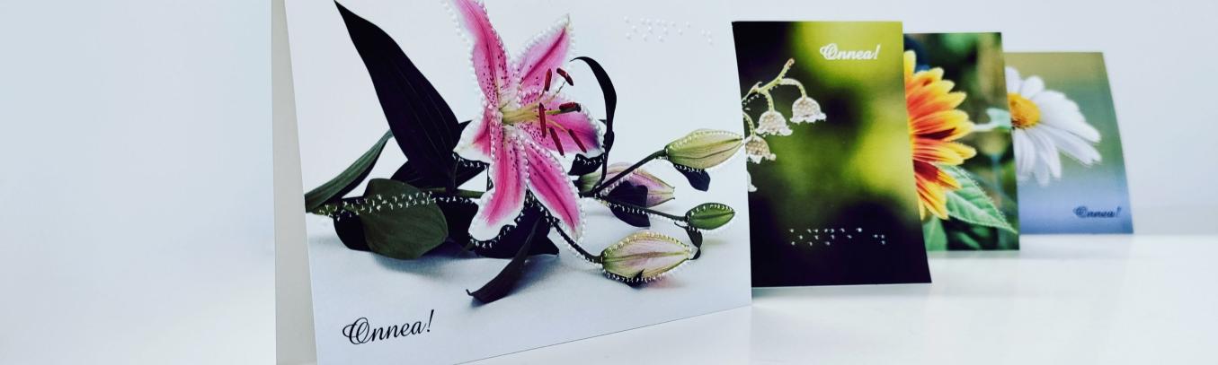 Neljä kaksiosaista postikorttia, joissa erilaiset kukkakuvat ja onnea-teksti. Kukkien ääriviivat ja teksti myös pisteillä.